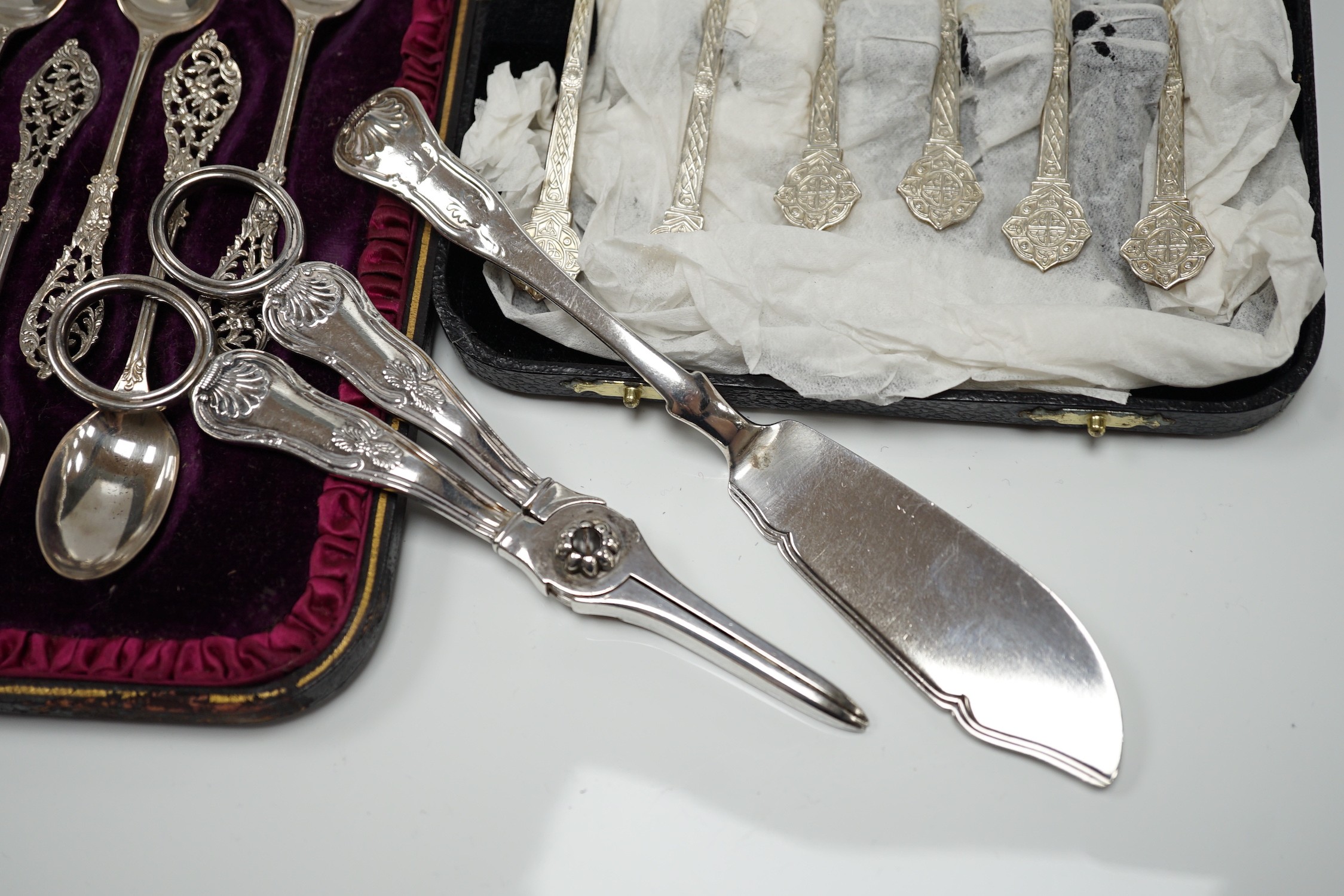 A cased set of twelve Victorian silver teaspoons, with pierced terminals by William Comyns, London 1889, with a damaged pair of matching sugar tongs, a cased set of six later teaspoons, a pair of George IV silver King's
